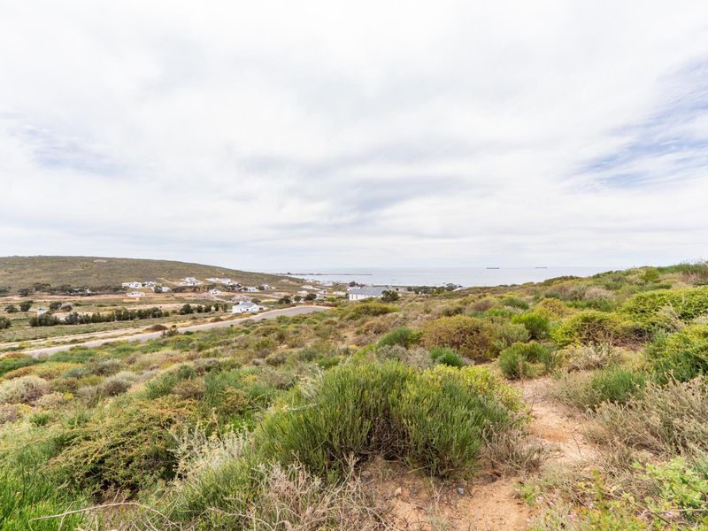 A wide-angle view of the vacant residential land featuring natural coastal vegetation, a nearby road, and distant ocean views.
