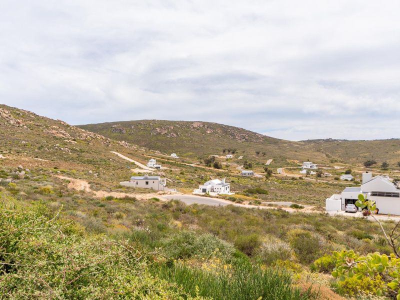 An elevated view of a residential estate featuring scattered modern homes set within a natural, hilly landscape with paved access roads.