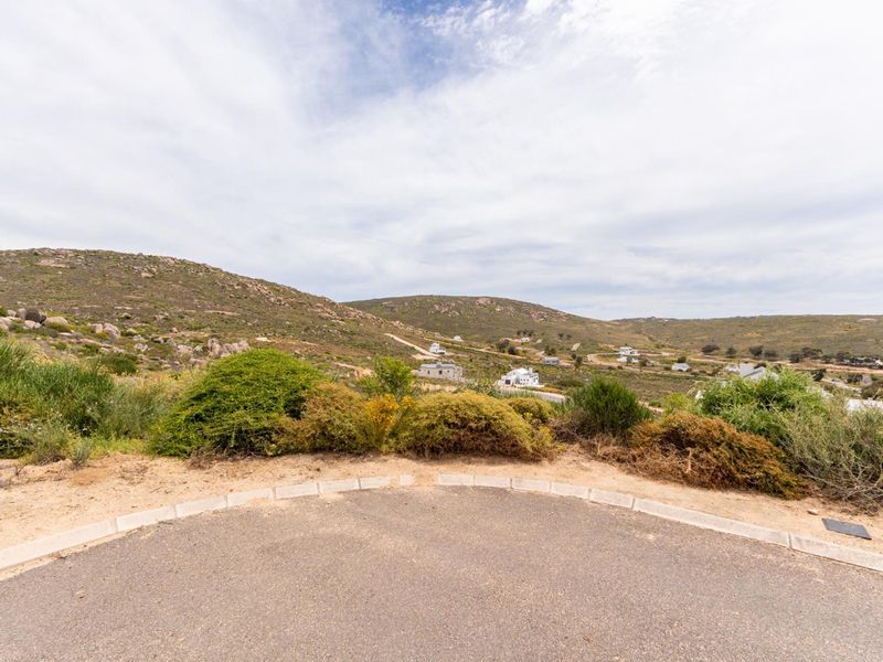 A scenic view overlooking the surrounding hilly landscape and residential area from a paved road.