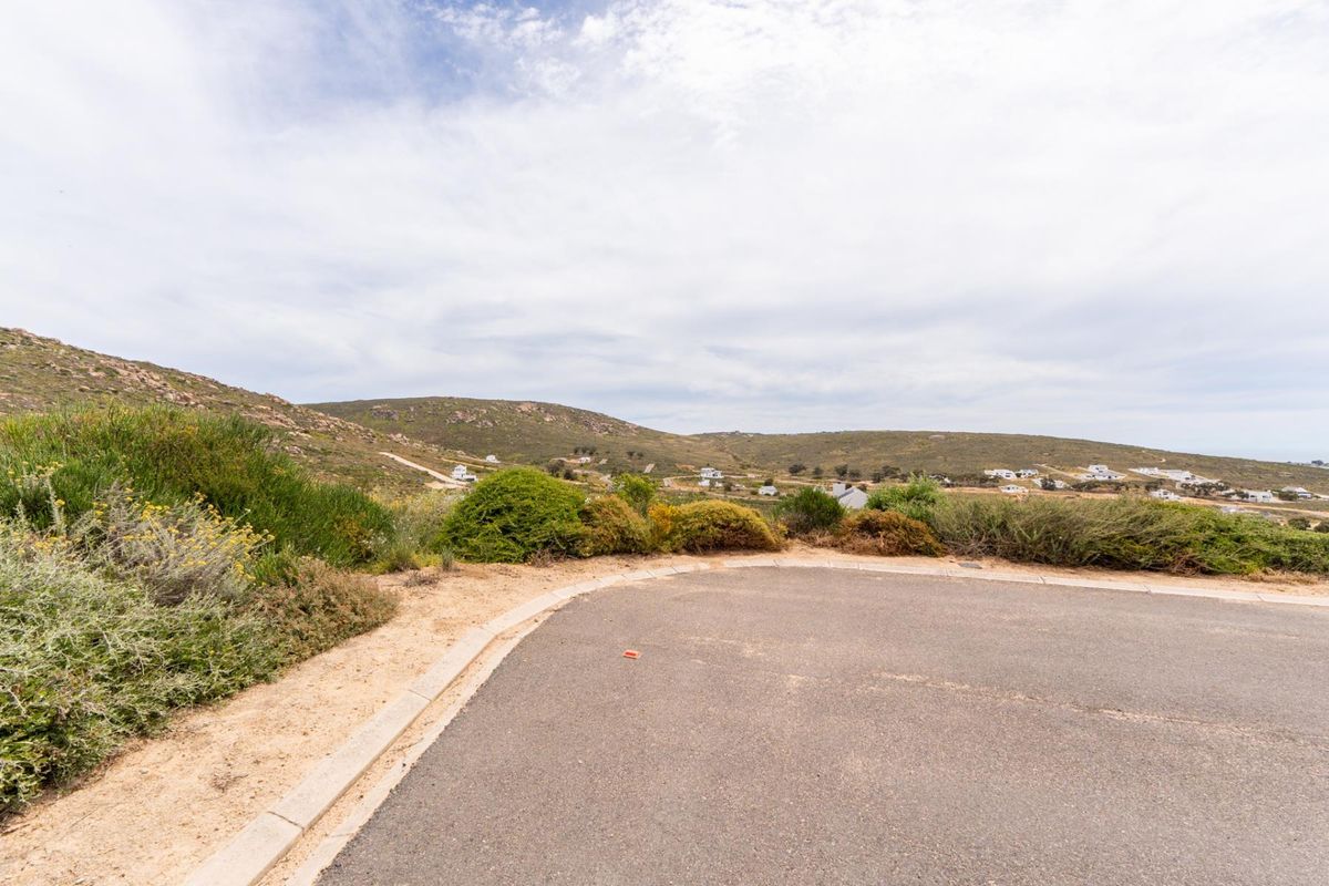 A view of the surrounding landscape and hilly terrain from the edge of a paved residential road.