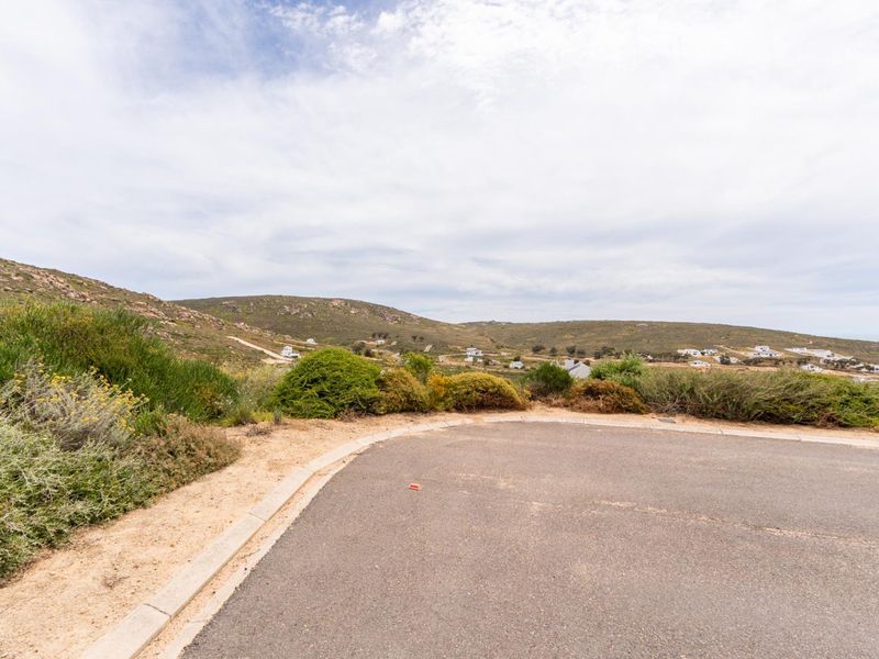 A view of the surrounding landscape and hilly terrain from the edge of a paved residential road.