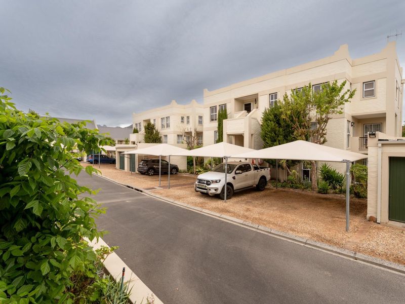 Exterior view of an apartment complex featuring covered parking bays, paved driveway access, and multi-story residential building facades.