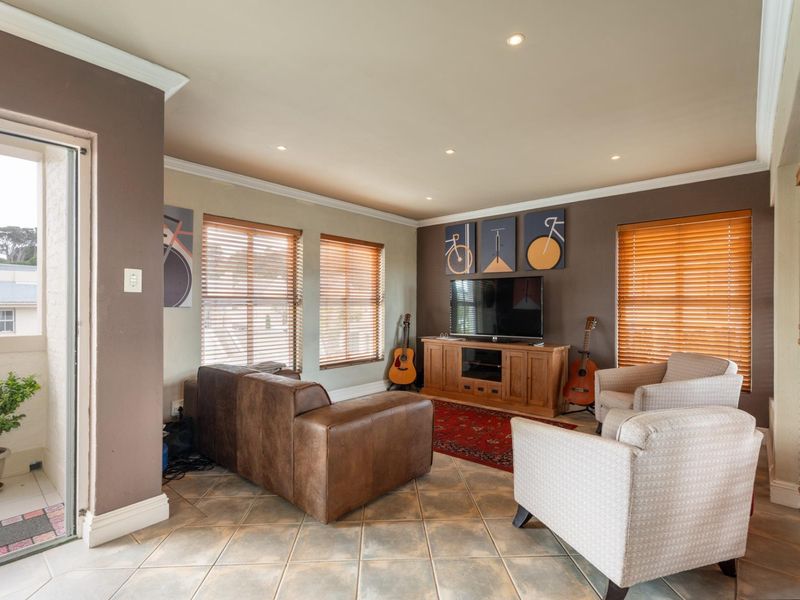 A comfortable living room featuring tiled flooring, recessed lighting, crown molding, and direct access to an outdoor balcony through a sliding glass door.
