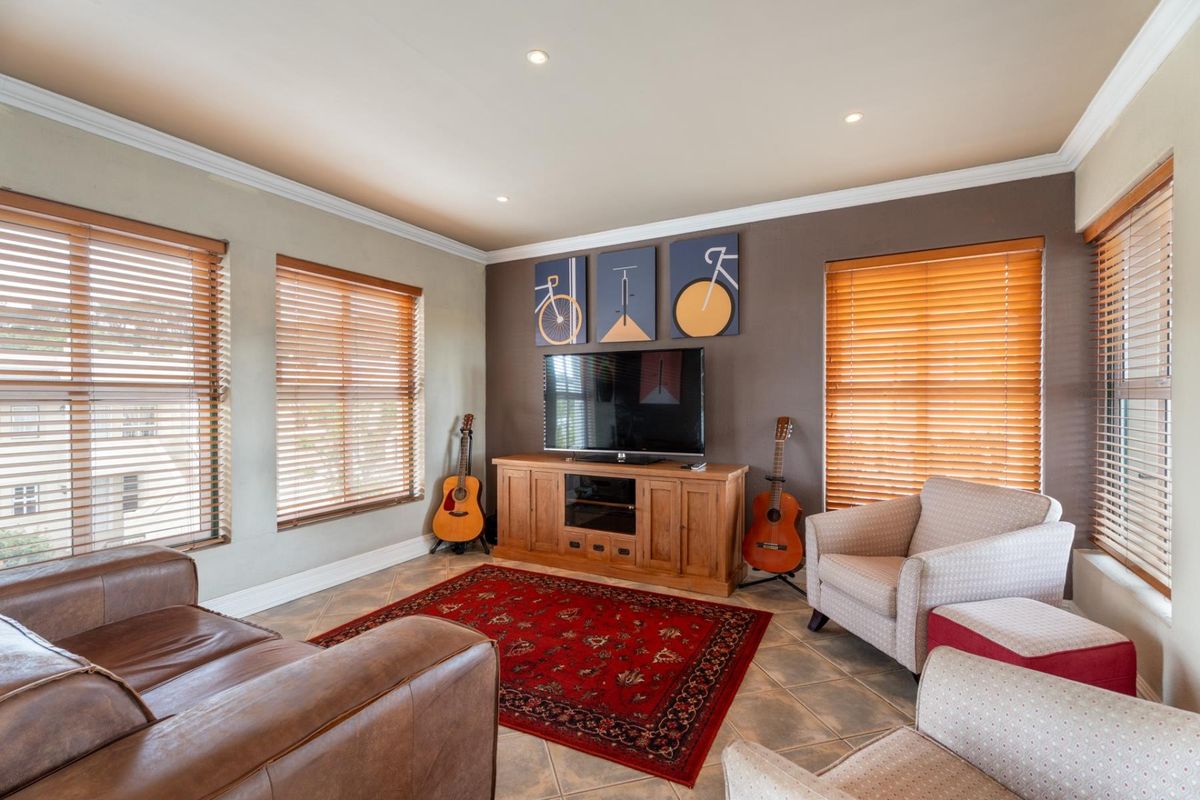A well-lit living room featuring tiled flooring, crown molding, recessed downlights, and multiple windows fitted with wooden venetian blinds.