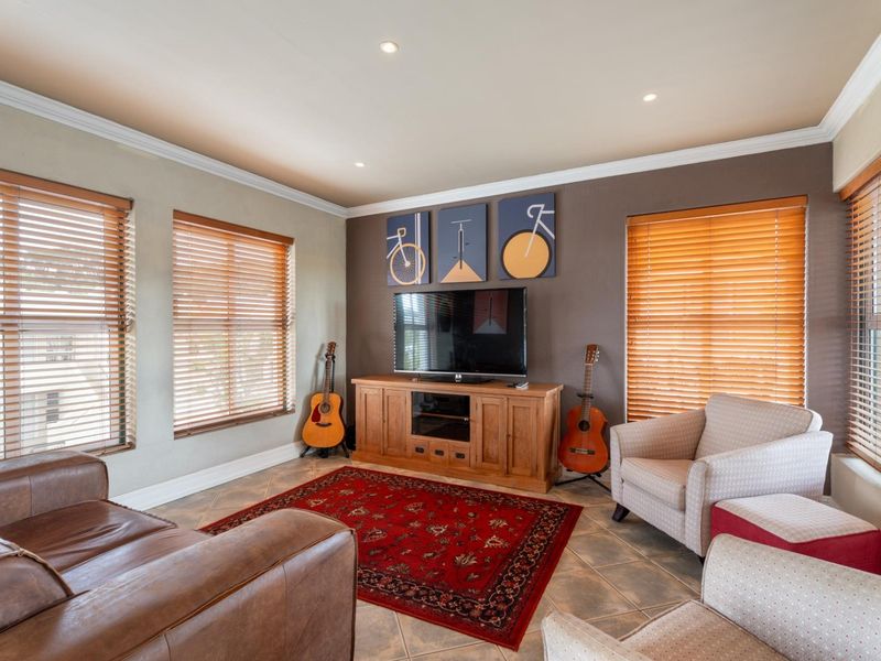 A well-lit living room featuring tiled flooring, crown molding, recessed downlights, and multiple windows fitted with wooden venetian blinds.