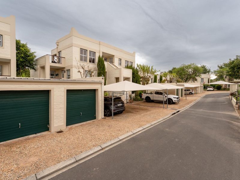 Exterior view of an apartment complex featuring a paved driveway, gravel parking area, and multiple garage units with covered carports.