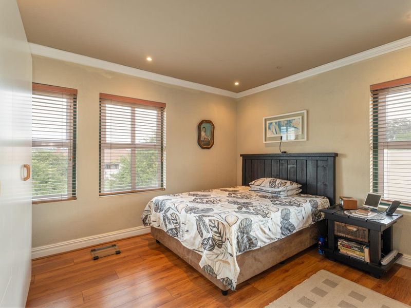 A well-maintained bedroom featuring warm timber flooring, recessed downlighting, built-in wardrobe storage, and venetian blinds for adjustable natural light.
