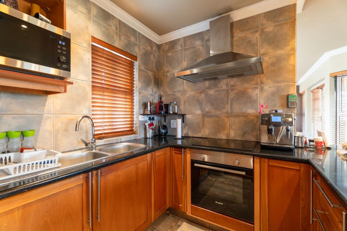 A functional kitchen featuring wooden cabinetry, granite countertops, a stainless steel double sink, built-in oven, electric hob, and a stainless steel extractor fan.