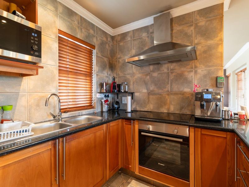 A functional kitchen featuring wooden cabinetry, granite countertops, a stainless steel double sink, built-in oven, electric hob, and a stainless steel extractor fan.