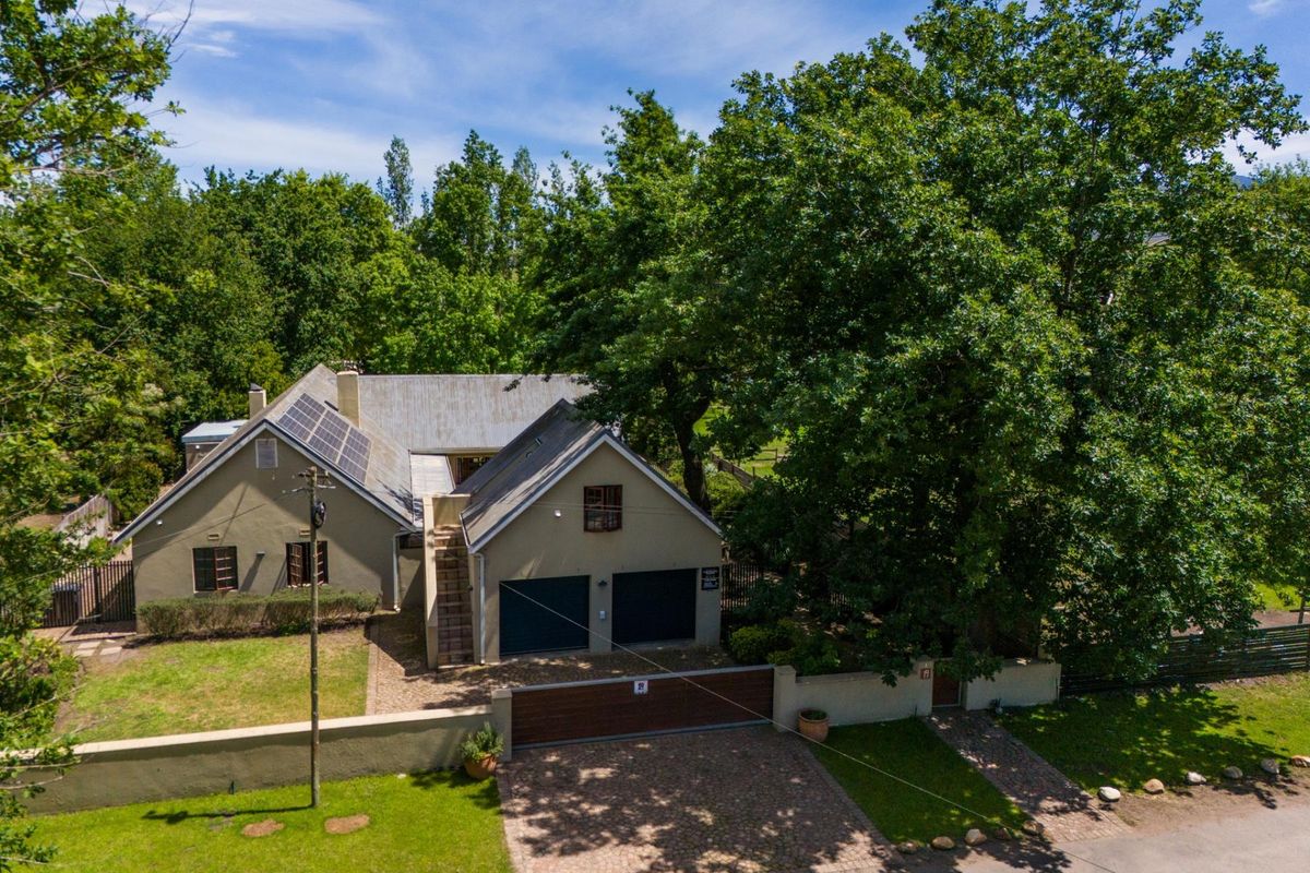 Aerial view of a residential property featuring a double garage, solar panels, paved driveway, and established garden surroundings.