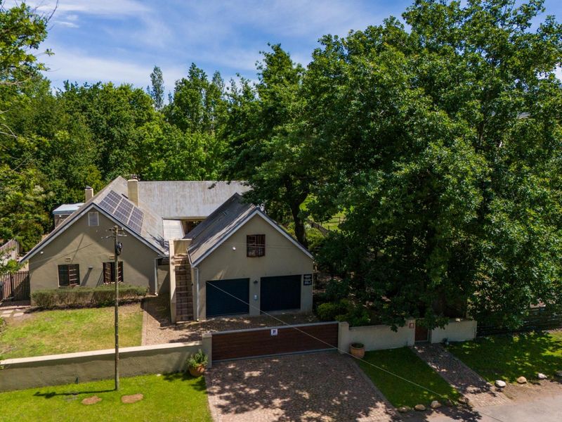 Aerial view of a residential property featuring a double garage, solar panels, paved driveway, and established garden surroundings.