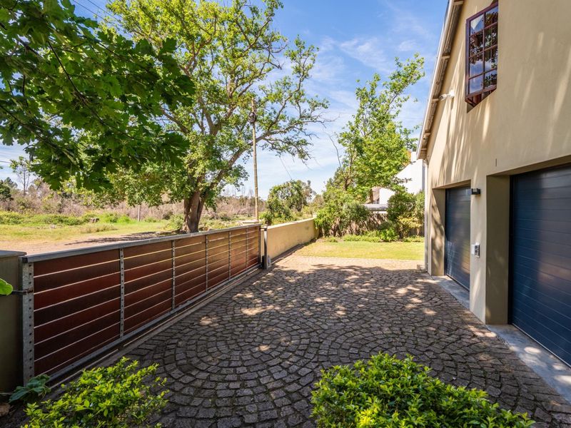 Front exterior view featuring a neat cobblestone driveway, automated sliding gate, and double garage access with surrounding garden space.