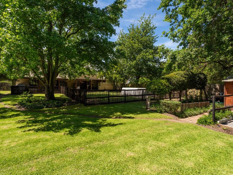 A spacious, well-maintained garden featuring mature trees, a lush lawn, wooden fencing, and a practical storage shed.