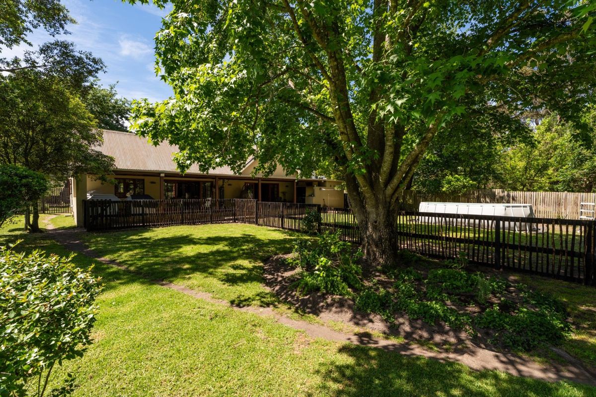 A spacious rear garden featuring a well-maintained lawn, mature trees, and a fenced-off area with a covered patio attached to the main house.