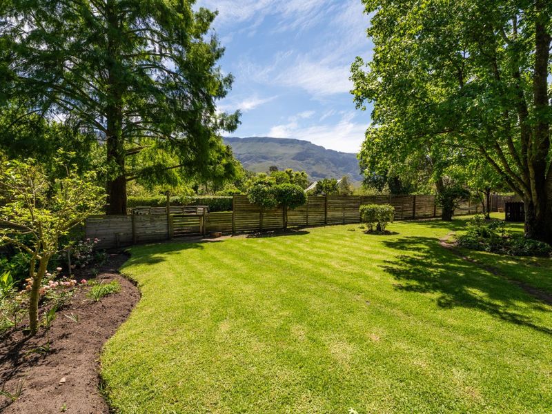 A well-maintained garden featuring a lush green lawn, mature trees, and timber boundary fencing with scenic mountain views in the background.