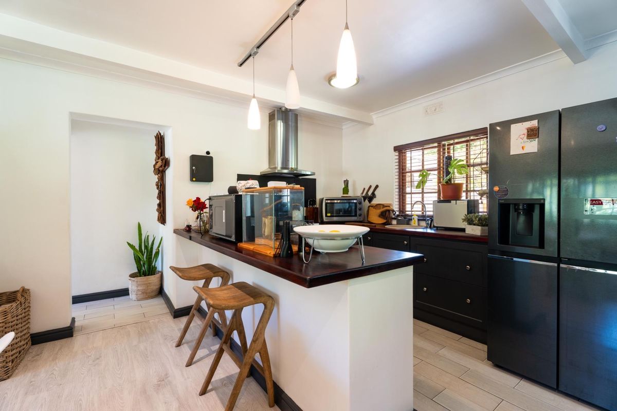 A functional kitchen featuring dark cabinetry, a wooden breakfast bar, stainless steel extractor fan, and modern track lighting with tiled flooring.