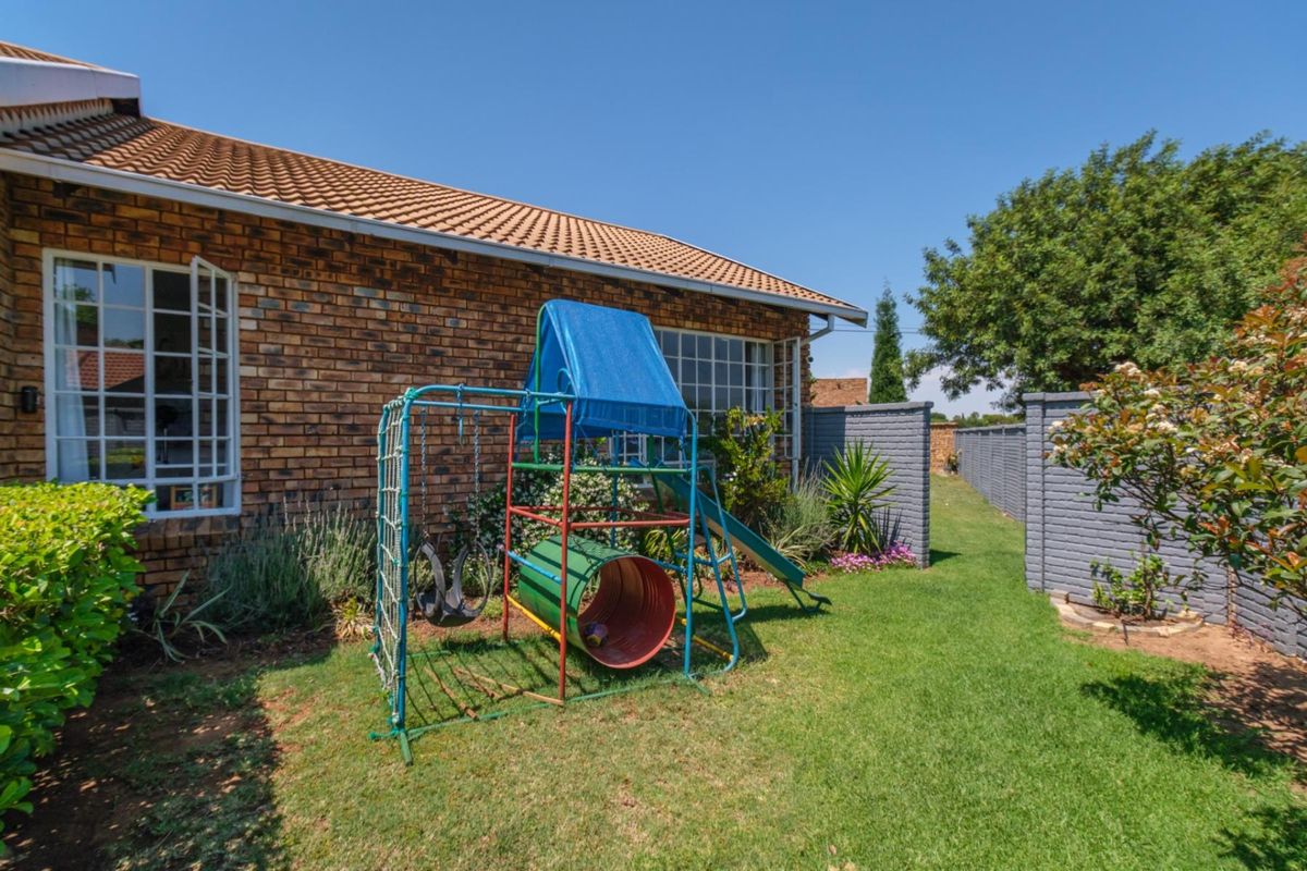 A view of the rear garden featuring a brick exterior wall, tiled roof, and perimeter boundary wall with a well-maintained lawn.