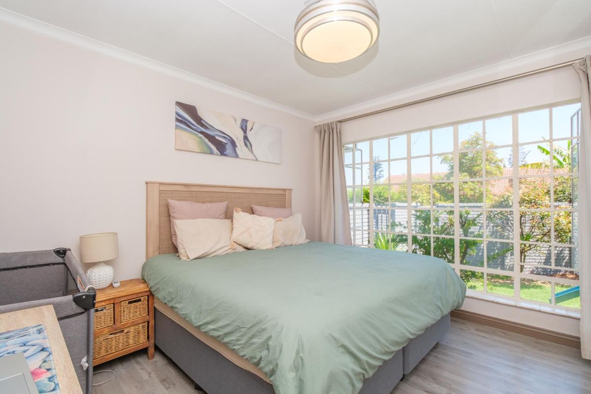 A bright bedroom featuring laminate flooring, a large grid-pattern window overlooking the garden, and a central ceiling light fixture.