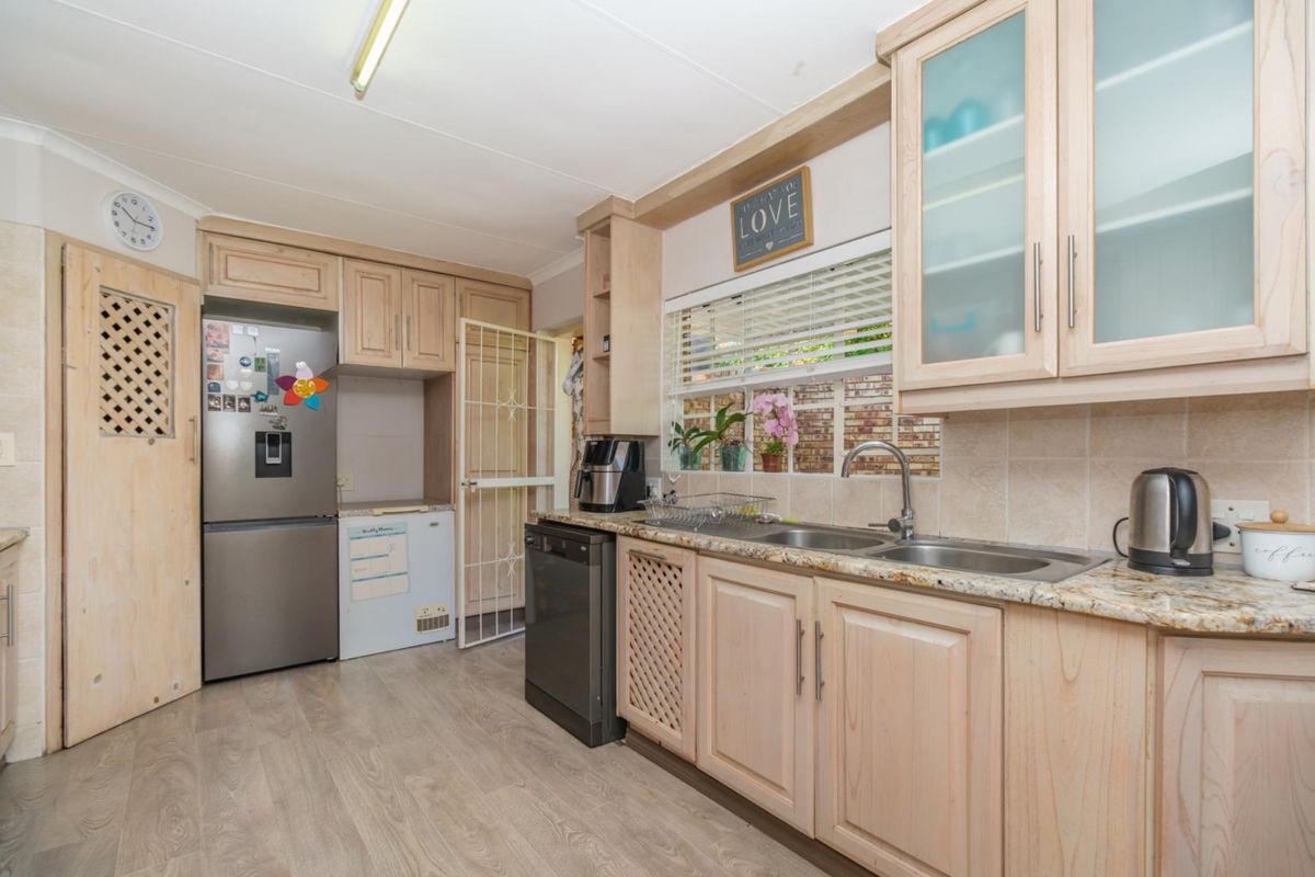 A functional kitchen featuring light wood cabinetry, granite countertops, a double stainless steel sink, and durable laminate flooring.