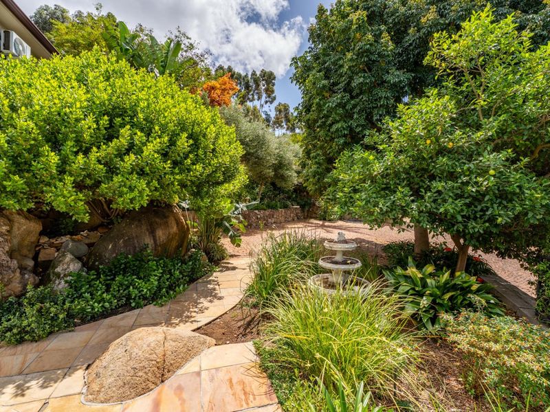 A beautifully landscaped garden featuring a stone paved pathway, mature trees, and a decorative water fountain, creating a serene outdoor environment.
