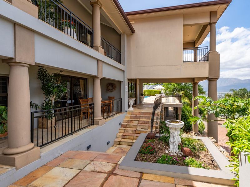 Spacious multi-level outdoor patio and balcony area featuring stone paving, wrought iron railings, and elegant concrete columns overlooking the garden and pool.