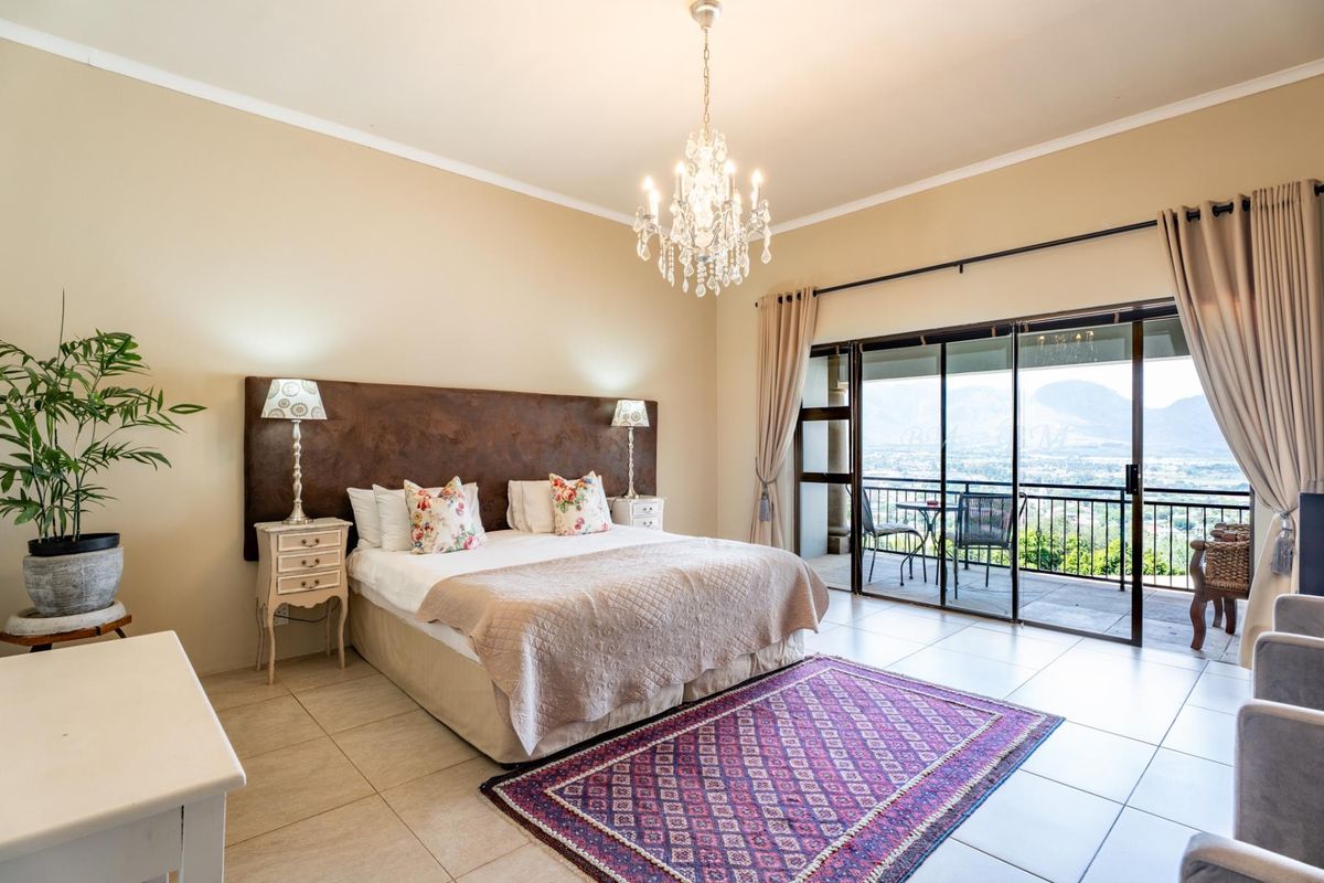 Spacious bedroom featuring tiled flooring, a decorative crystal chandelier, and large sliding glass doors that open onto a private balcony with scenic mountain views.