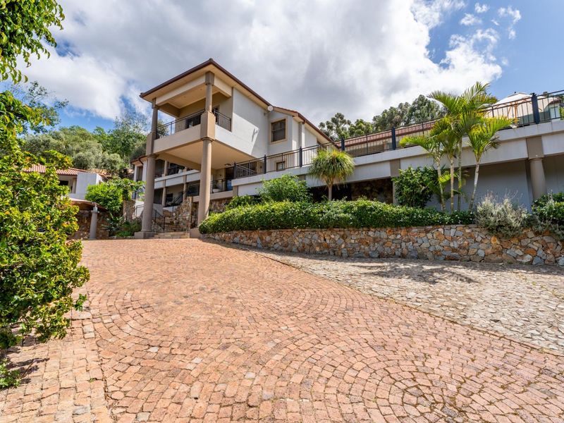 A well-maintained multi-level house featuring a cobblestone driveway, stone retaining walls, and an elevated balcony with metal railings.