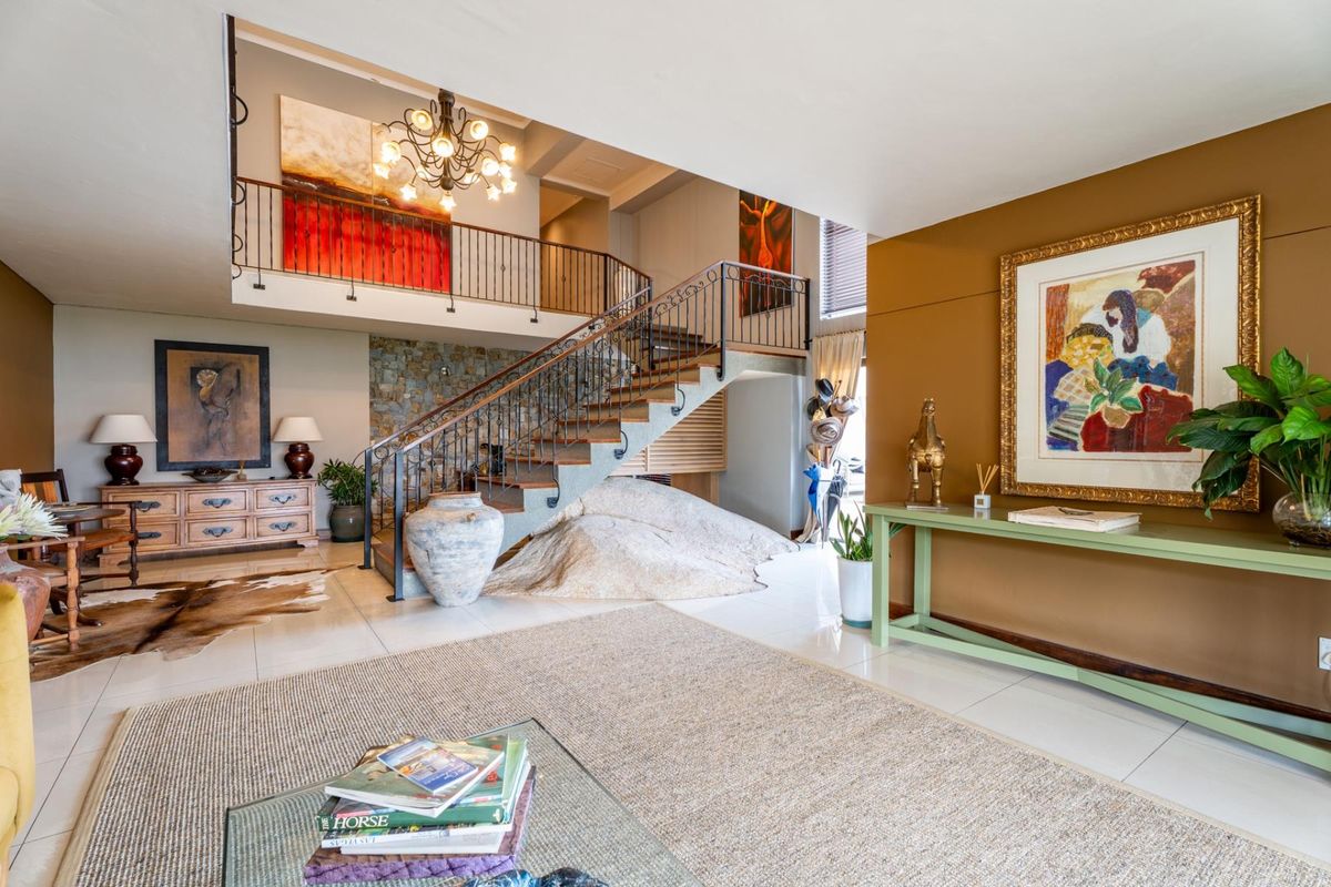 Spacious living area featuring a grand staircase with wrought iron balustrade, stone feature wall, and an open mezzanine landing with elegant lighting.