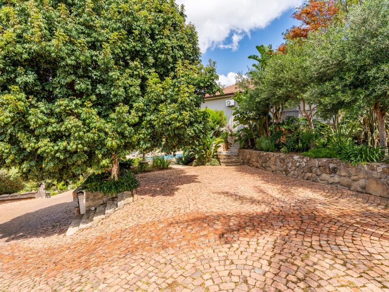 A well-maintained front exterior featuring a charming cobblestone driveway, stone retaining walls, and mature landscaping providing a private and inviting entrance.