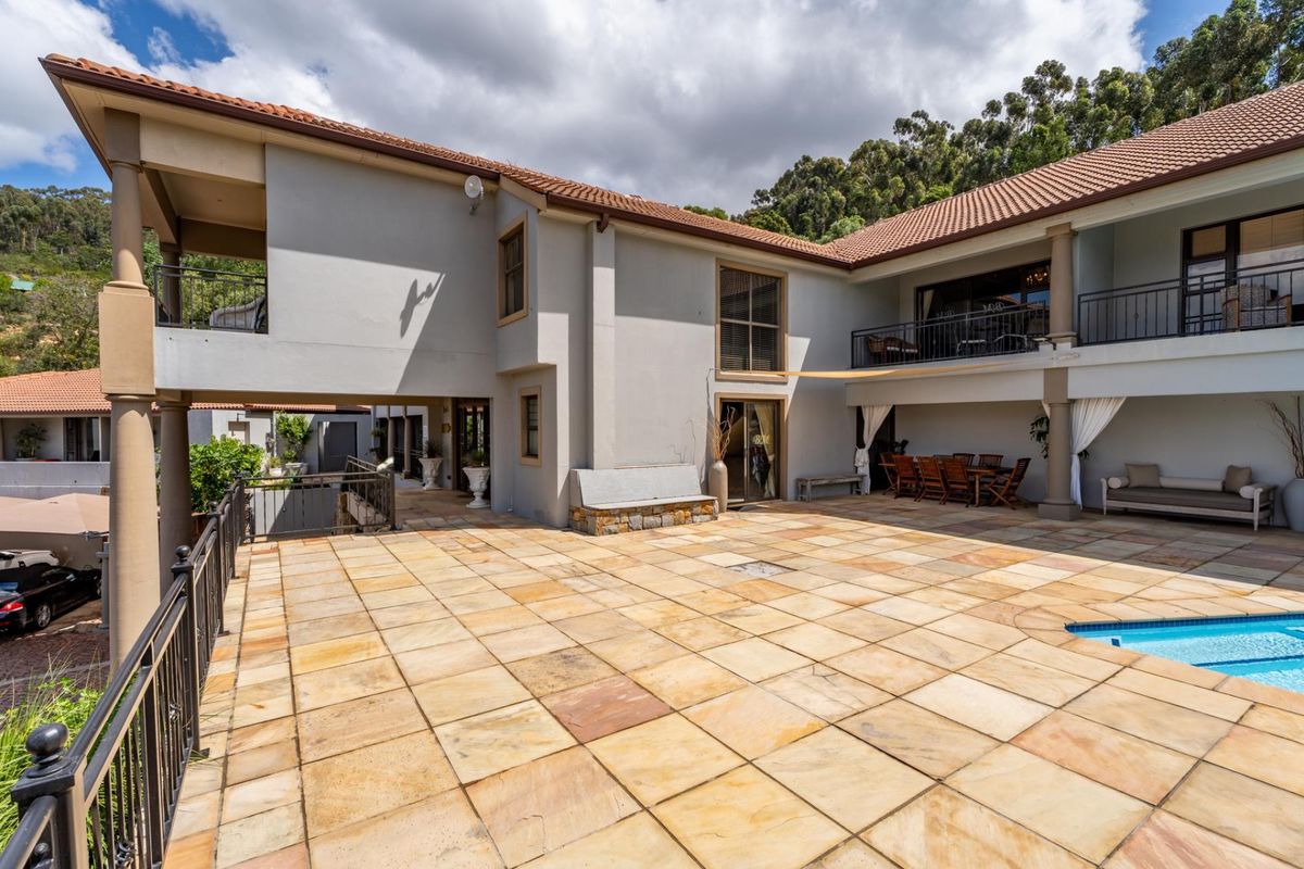 Spacious rear exterior featuring a large stone-paved patio, swimming pool, and covered balcony areas with wrought iron railings.