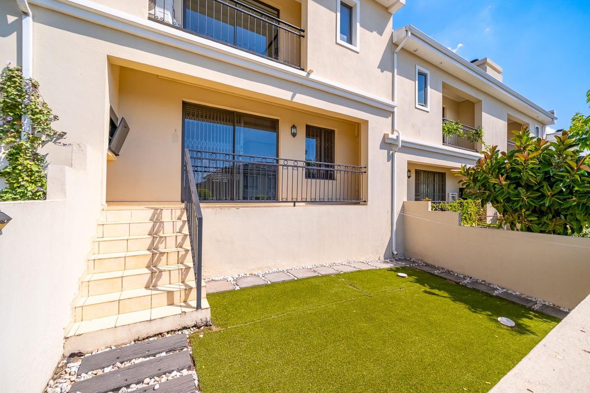 Rear view of the apartment featuring a private garden with artificial lawn, tiled staircase, and a balcony with metal balustrades.