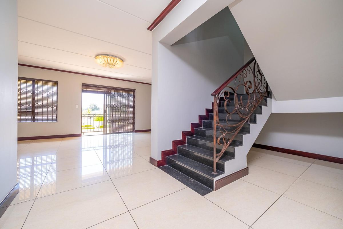 Spacious open-plan living area featuring polished tile flooring, a striking staircase with wrought iron balustrade, and direct access to an outdoor balcony.