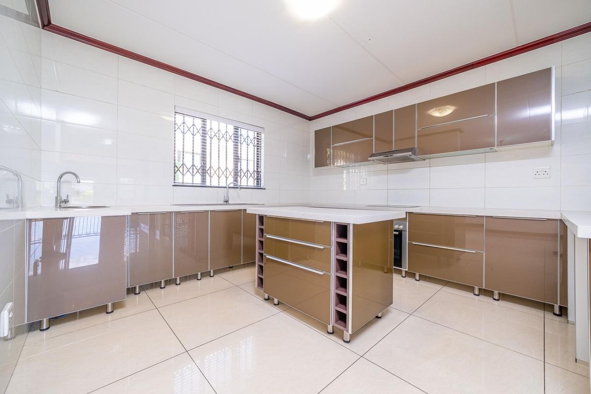 Modern kitchen featuring high-gloss cabinetry, a central island, built-in oven, extractor fan, and tiled finishes throughout.