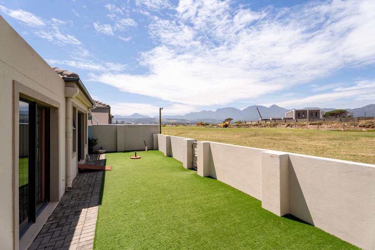 Rear exterior view featuring a low-maintenance artificial grass lawn, paved walkway, and boundary wall with scenic mountain views in the background.