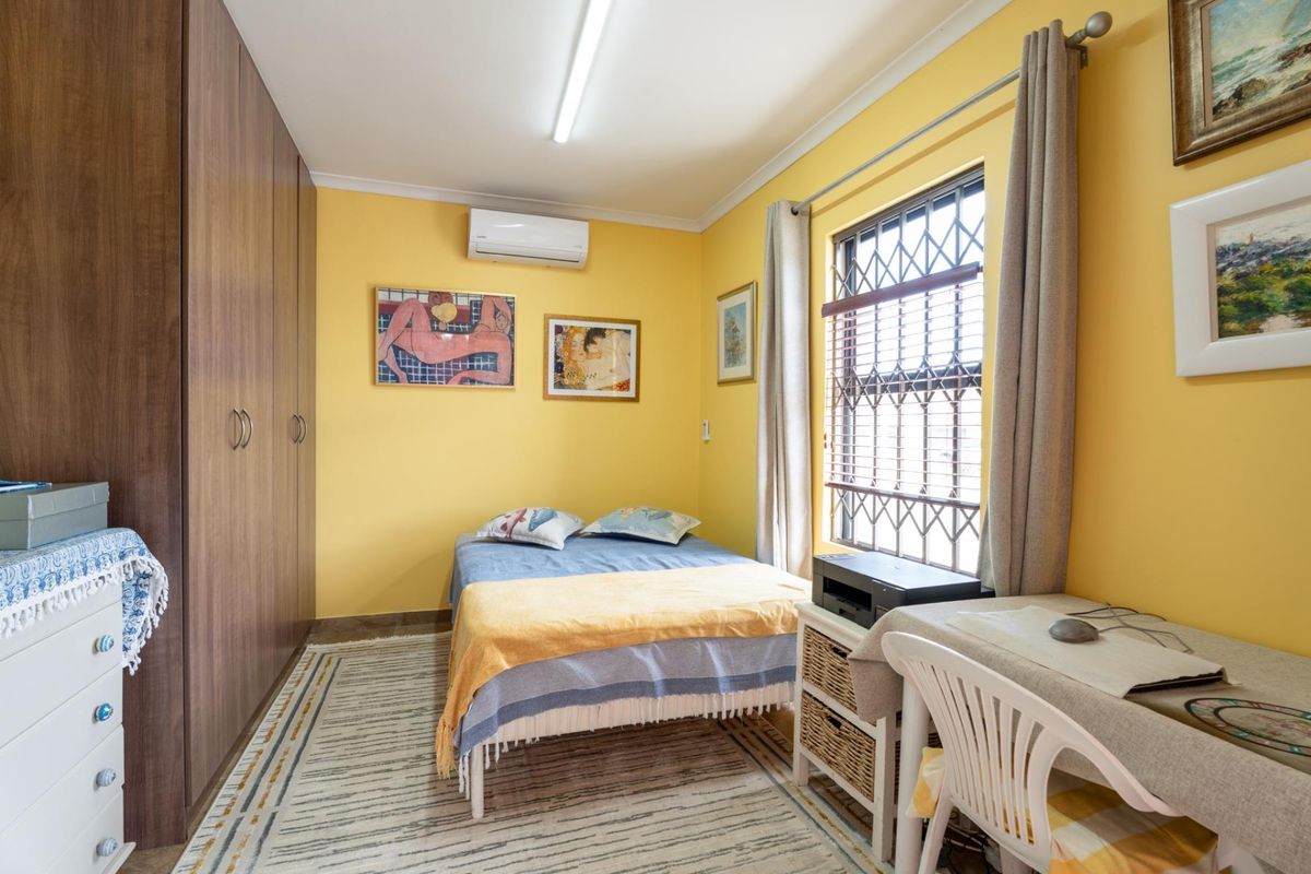 A functional bedroom featuring built-in wooden cupboards, a split-system air conditioner, and a window fitted with a security gate.