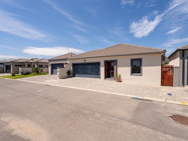 Front elevation of a modern single-story house featuring a paved driveway, double garage, and tiled roof in a well-maintained residential street setting.