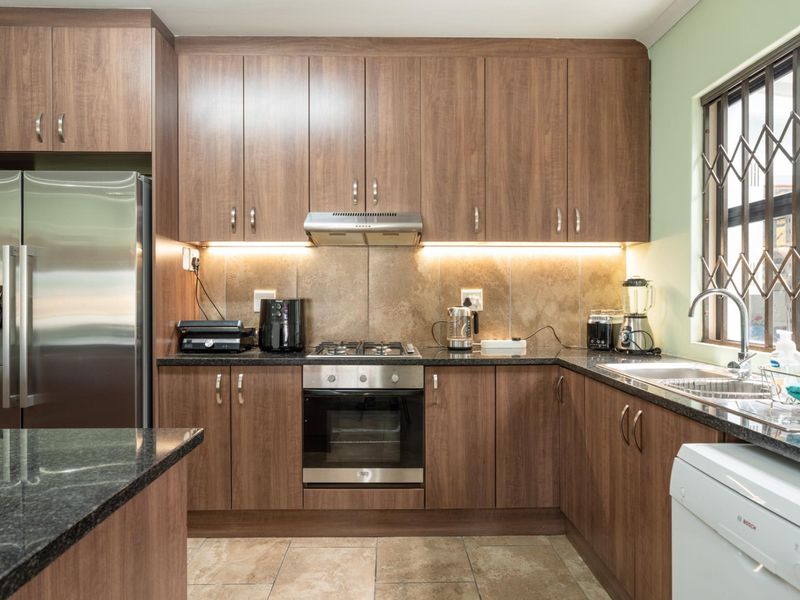 A well-maintained kitchen featuring wood-finish cabinetry, granite countertops, integrated gas hob, oven, and extractor fan with under-cabinet lighting.