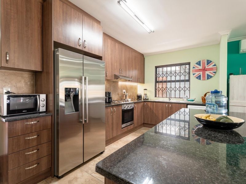 Modern kitchen featuring dark wood cabinetry, granite countertops, a central island, and integrated stainless steel appliances, offering a functional and well-maintained cooking space.