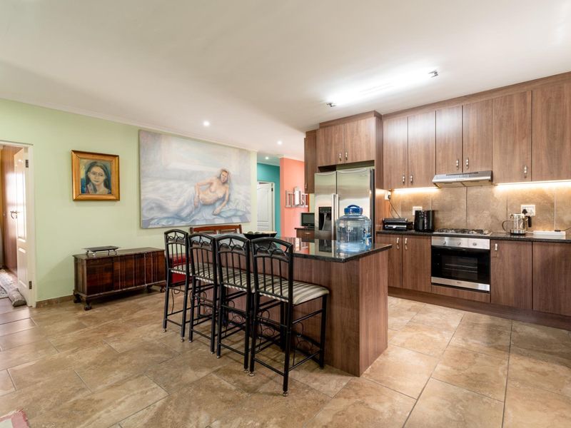 Open-plan kitchen featuring wood-finish cabinetry, granite countertops, a central island, and tiled flooring, seamlessly integrated with the living area.