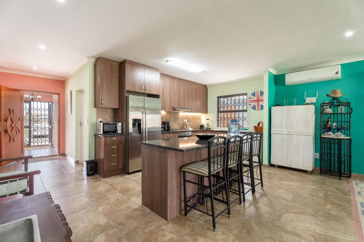Spacious open-plan kitchen featuring dark wood cabinetry, granite countertops, a central island, and tiled flooring, seamlessly connecting to the home entrance.