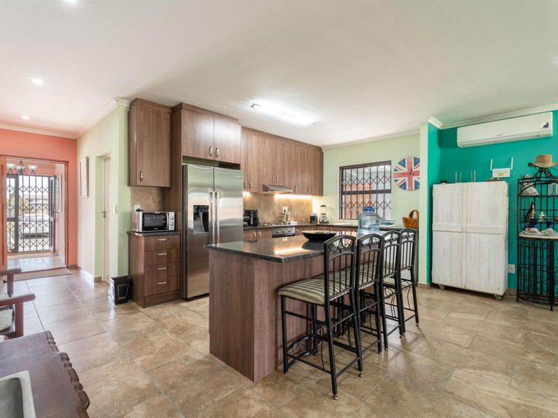 Spacious open-plan kitchen featuring dark wood cabinetry, granite countertops, a central island, and tiled flooring, seamlessly connecting to the home entrance.