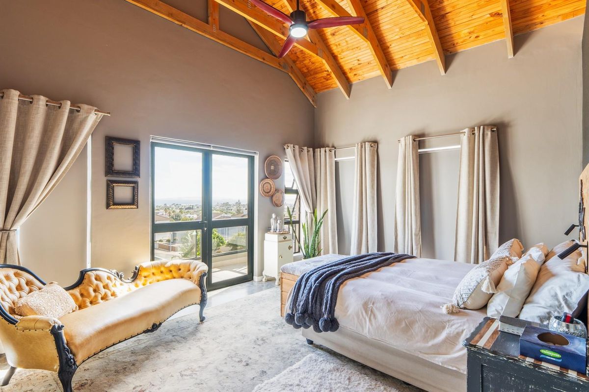 Spacious bedroom featuring high vaulted timber ceilings, exposed beams, and large glass doors opening to a balcony with scenic views.