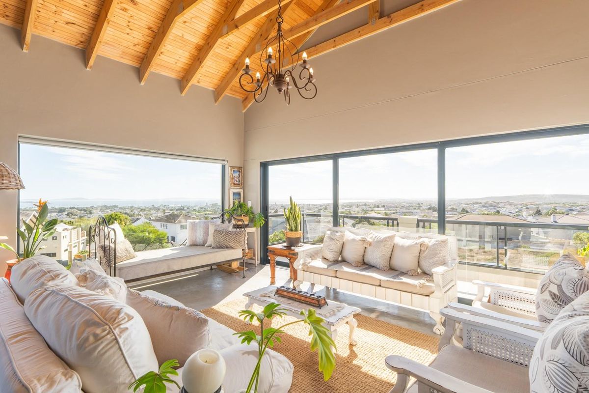 Spacious living area featuring high vaulted timber ceilings, polished concrete floors, and expansive sliding glass doors offering panoramic coastal and neighbourhood views.