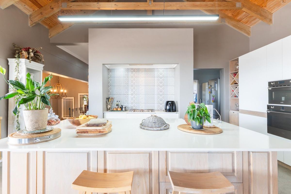 Modern kitchen featuring a large central island, built-in double ovens, and exposed timber roof trusses, creating a bright and spacious culinary area.