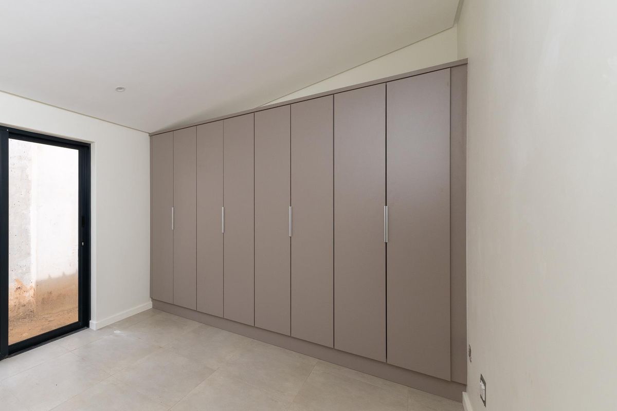 A modern bedroom featuring extensive built-in floor-to-ceiling cabinetry with a neutral finish and large glass door leading to an outdoor area.