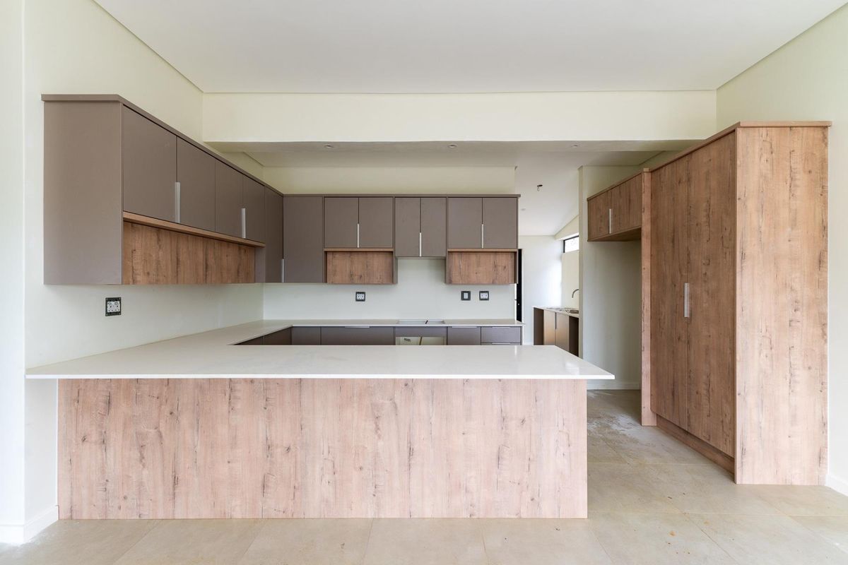 Modern kitchen featuring two-tone cabinetry, stone countertops, and a breakfast bar, with an adjacent scullery area visible in the background.