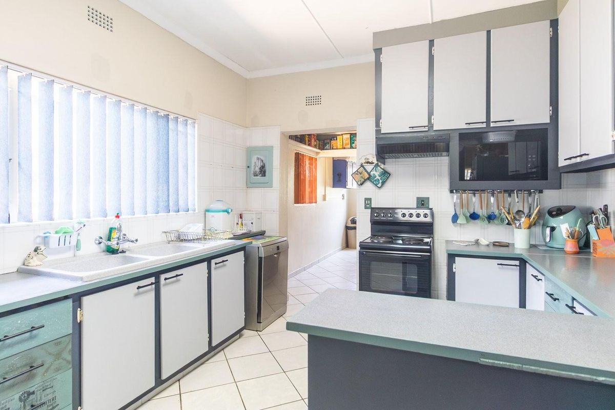 A functional kitchen featuring built-in cabinetry, a freestanding stove with extractor fan, double sink, and tiled flooring with access to an adjacent utility area.