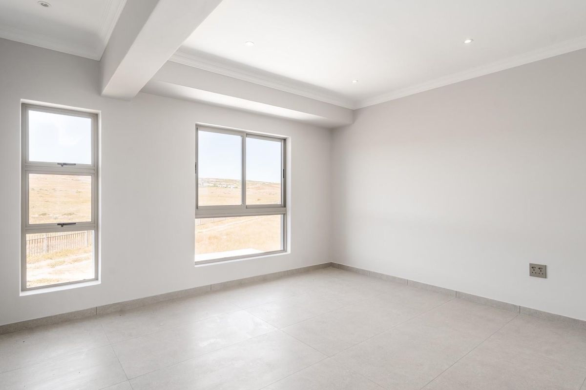 A bright, empty bedroom featuring neutral tiled flooring, recessed ceiling lighting, and large windows providing natural light and scenic views.