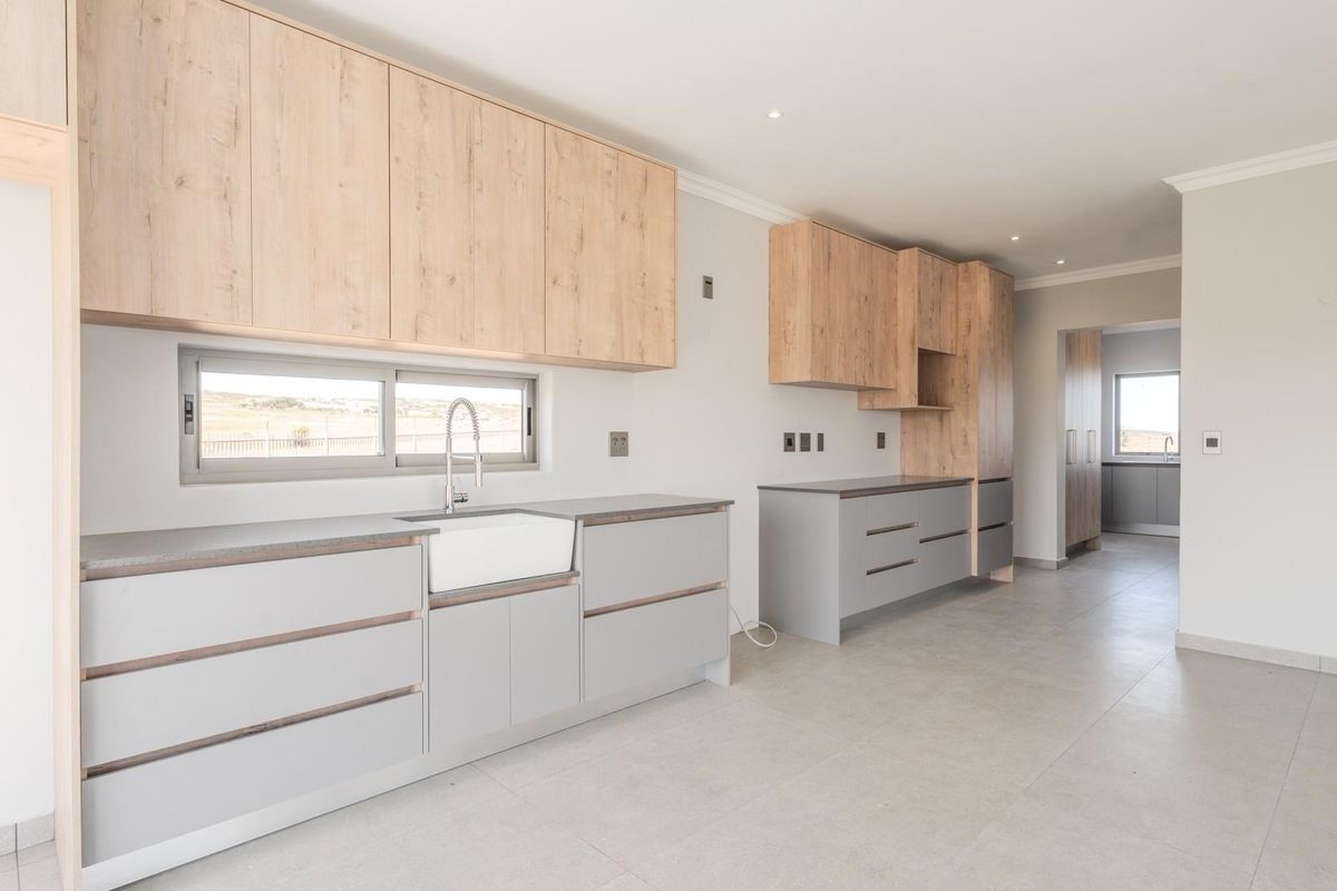 Modern kitchen featuring light wood-grain cabinetry, grey base units, a farmhouse-style sink, and tiled flooring in a clean, open-plan layout.