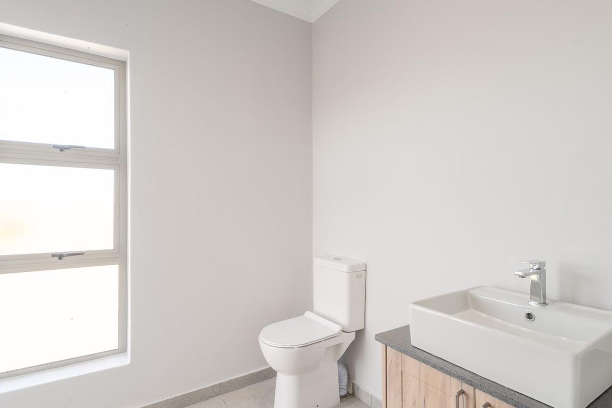 A clean and modern bathroom featuring a white toilet, a contemporary vessel sink set on a wooden vanity, and a large window.